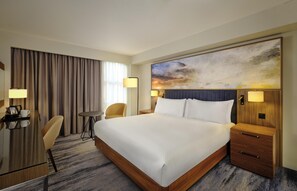 A hotel room with a large bed, bedside tables, a desk with a chair, a small round table, and a large abstract painting on the wall. - DoubleTree by Hilton Lincoln (Lincoln)