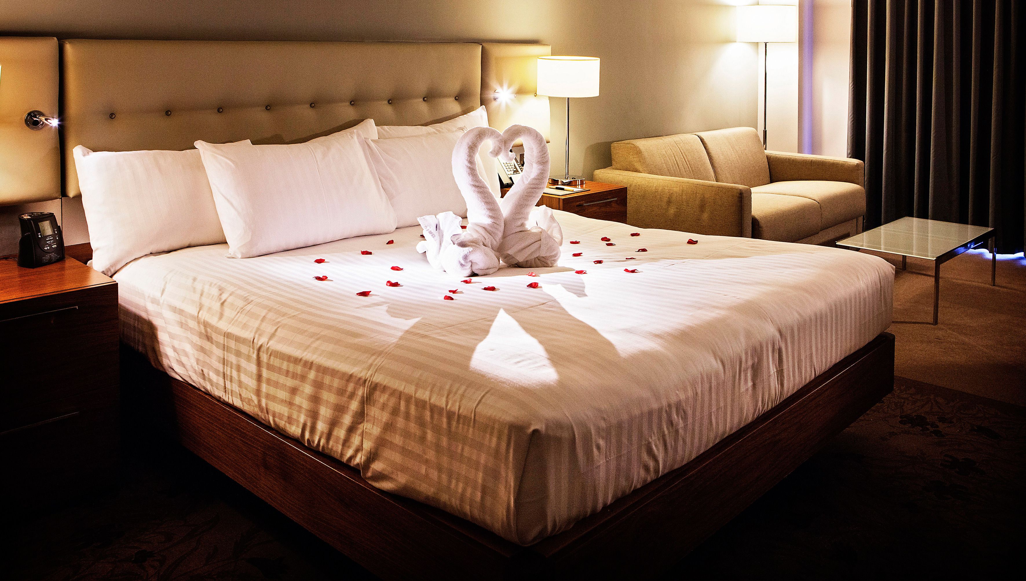 Quarto de hotel com uma cama grande, uma mesa de cabeceira com abajur, uma cadeira e uma pequena mesa.