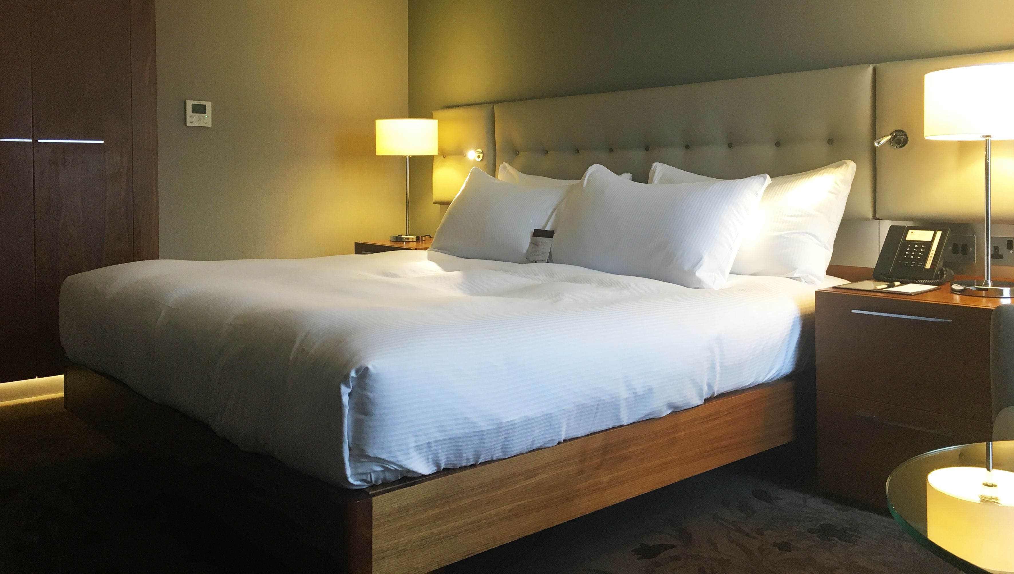 A neatly made bed with white linens, a wooden headboard, and two bedside tables with lamps and a telephone.