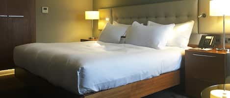 A neatly made bed with white linens, a wooden headboard, and two bedside tables with lamps and a telephone.