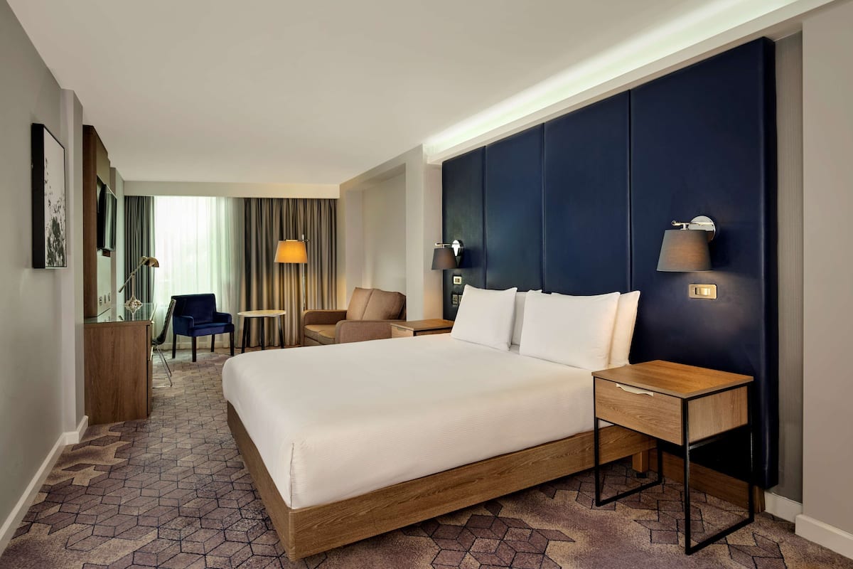 A hotel room with a large bed, a wooden nightstand, a desk, and a chair.