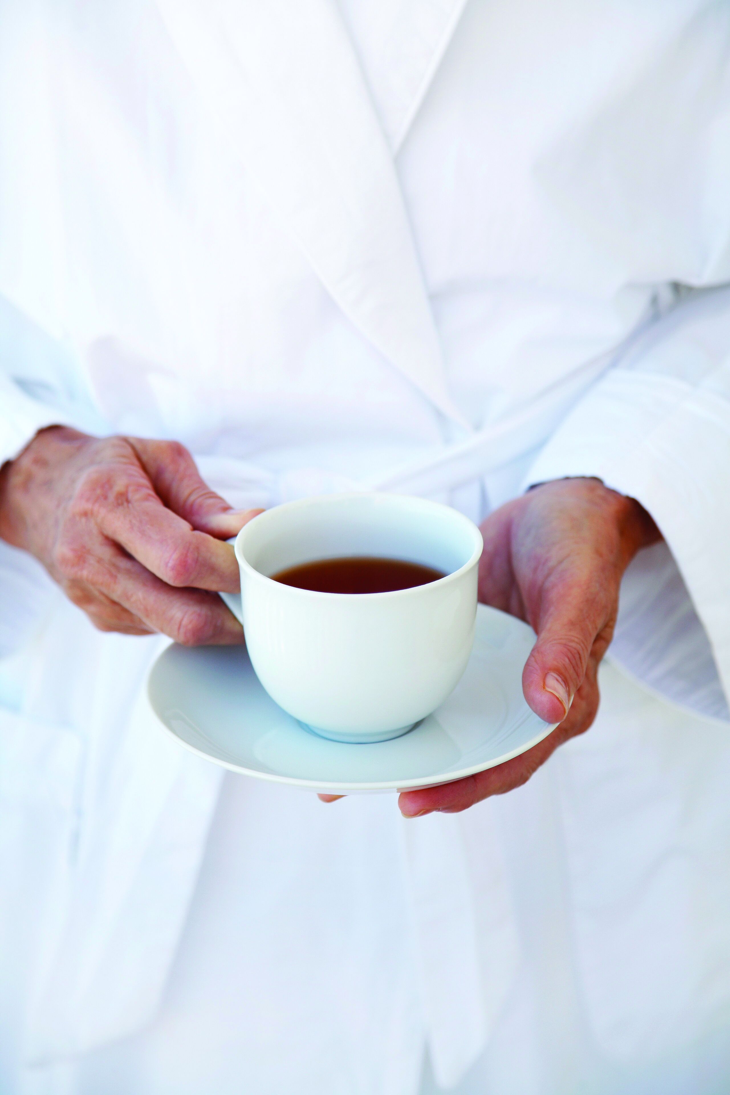 A person holding a white cup of tea on a saucer.