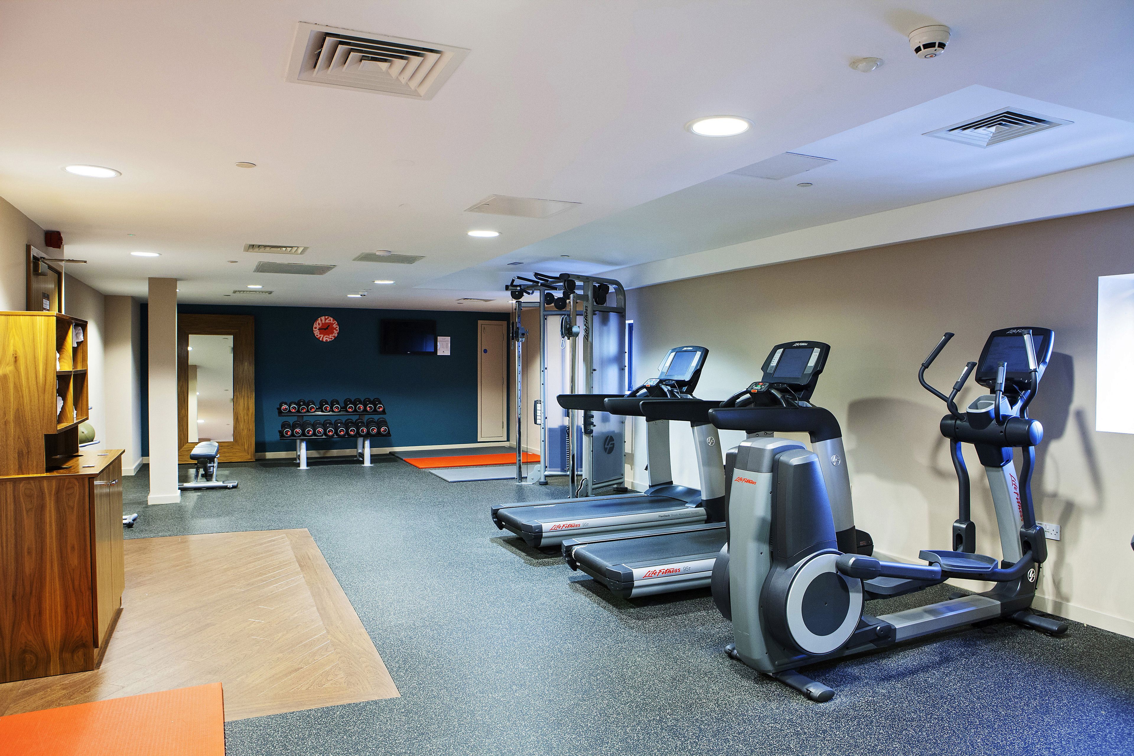 Une salle de sport équipée de tapis de course, de vélos elliptiques et d’une zone avec des bancs de musculation.