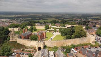 Um castelo histórico com um pátio central, rodeado por edifícios residenciais e um extenso campo aberto ao fundo.