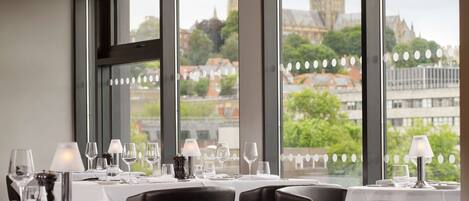 Een restaurant met gedekte tafels, grote ramen met uitzicht op een historisch gebouw.