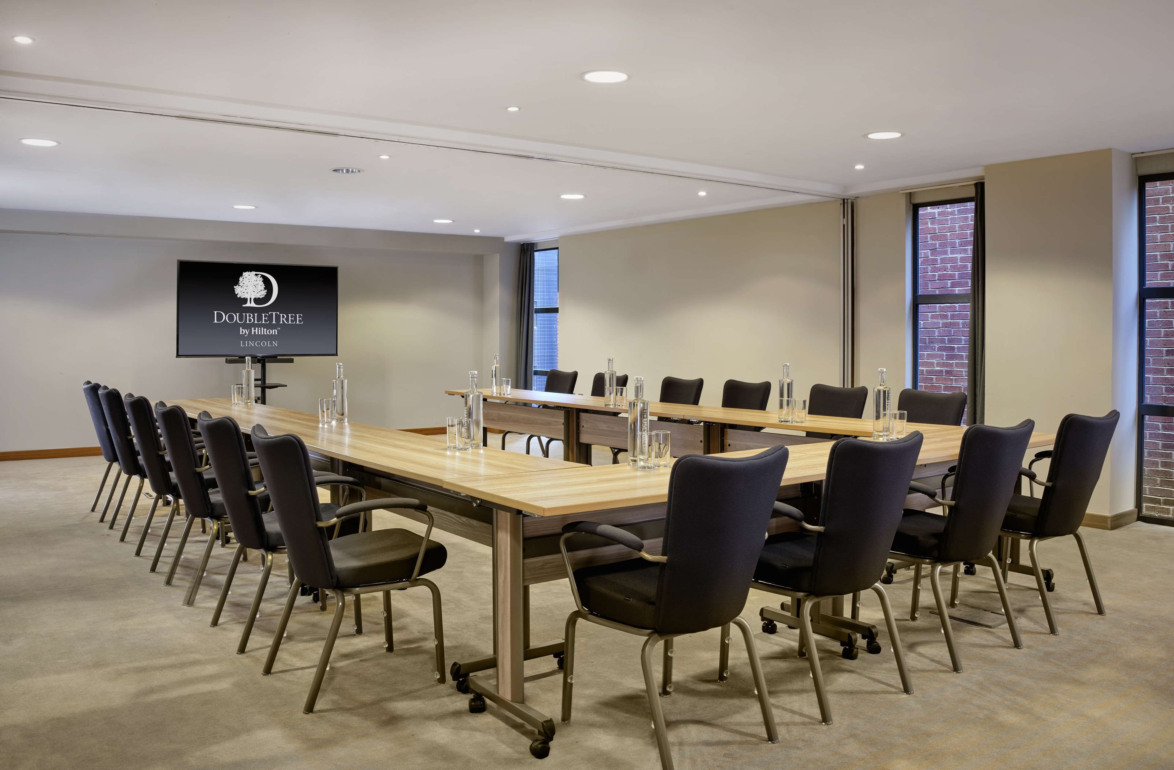 A conference room with a long table, chairs, a TV screen, and a brick wall.