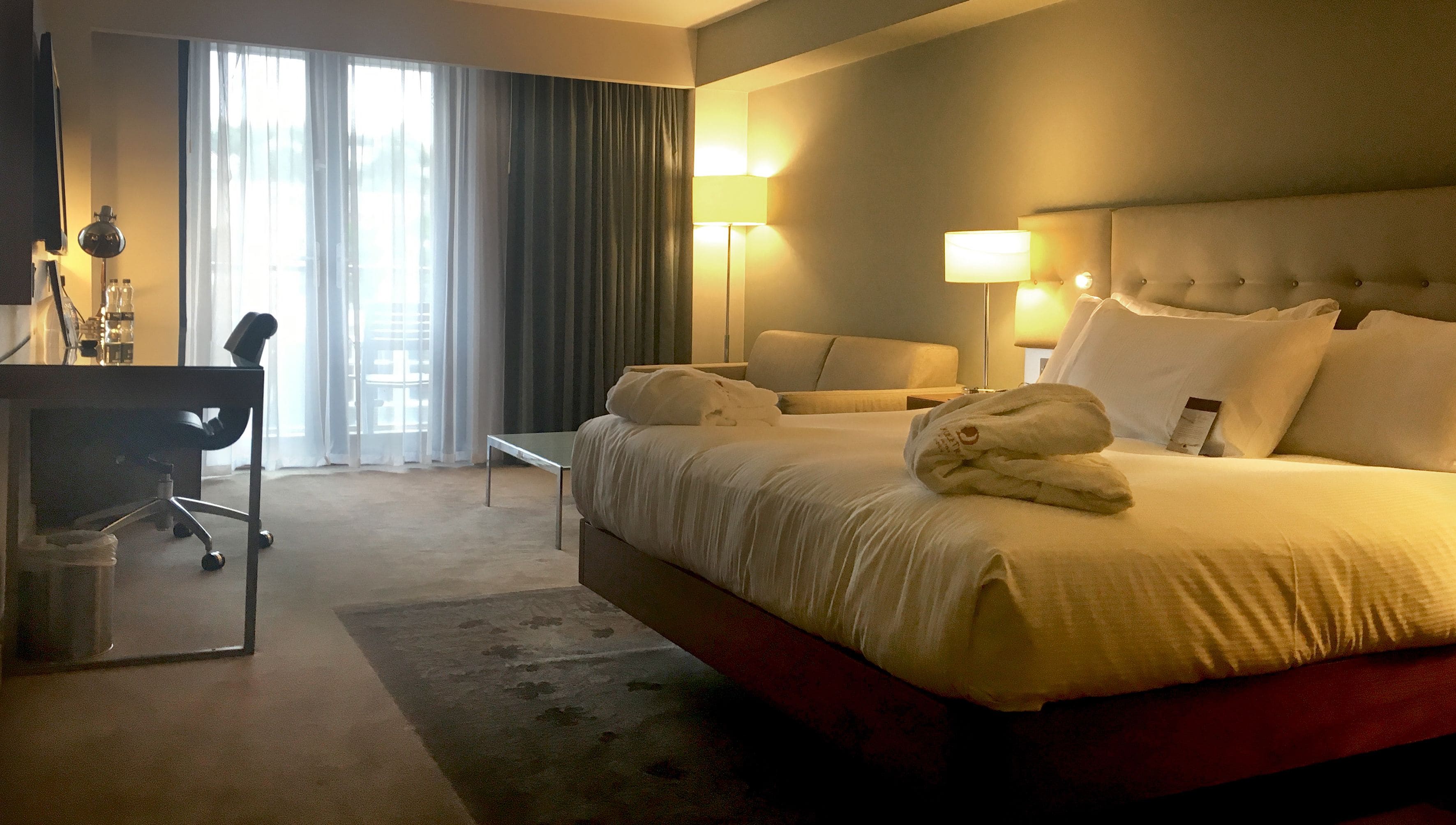 Habitación de hotel con una cama grande, dos lámparas de noche, un escritorio con una silla y vistas por la ventana.