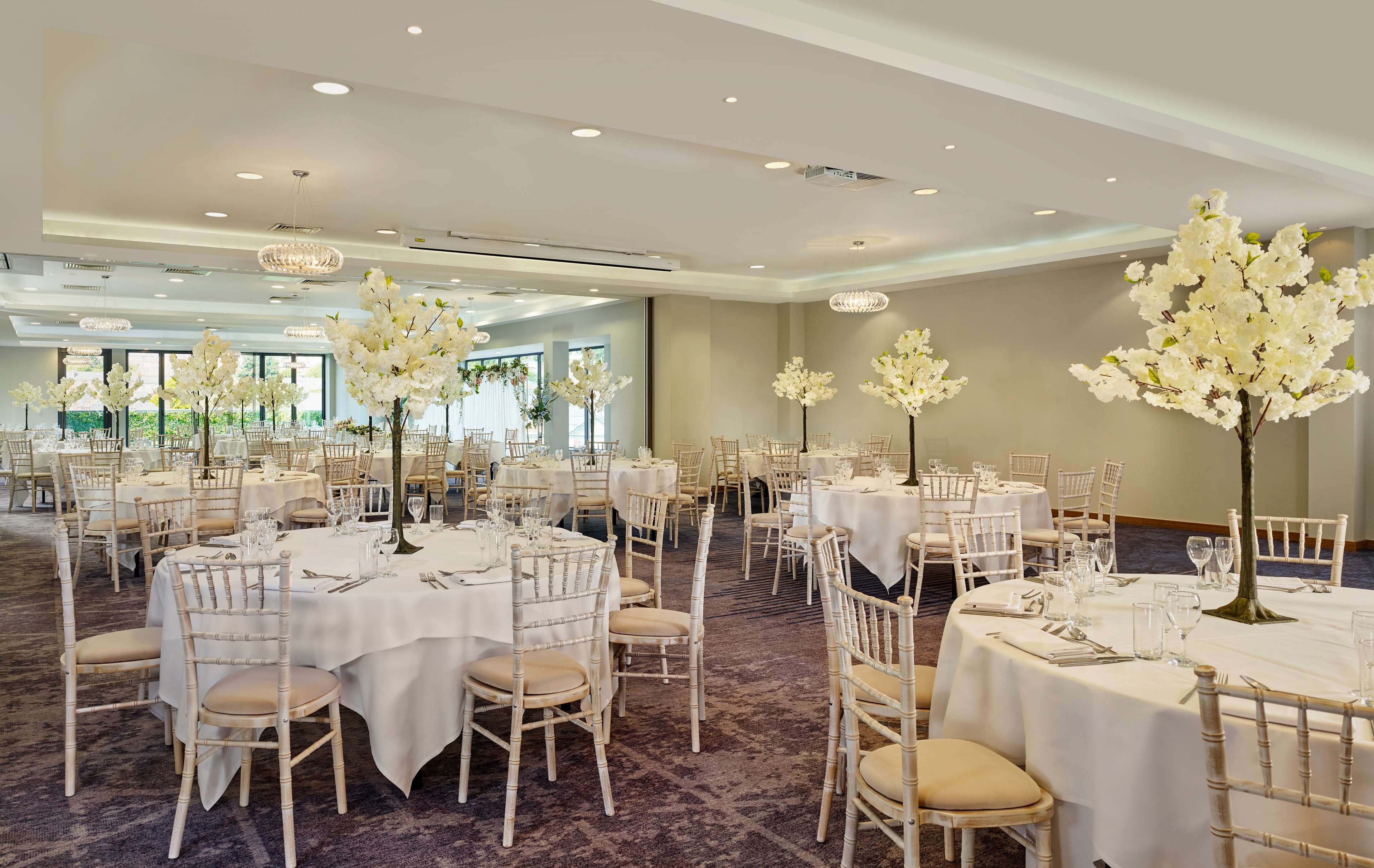 A banquet hall with round tables, white tablecloths, and tall floral centerpieces.