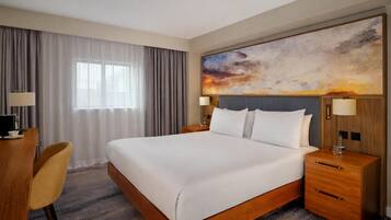 Habitación de hotel con una cama grande, un escritorio con silla, una mesita de noche con lámpara y un cuadro abstracto de gran tamaño en la pared.