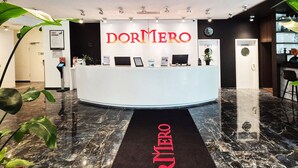 A reception desk with a sign reading "DORMERO" in a modern hotel lobby with marble flooring and potted plants. - Dormero Hotel Frankfurt Messe (Frankfurt)