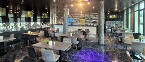Um restaurante moderno com piso de mármore, vários espaços de estar e cozinha visível ao fundo.
