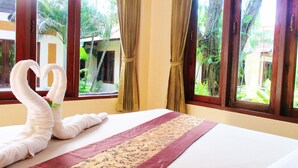A hotel room with a bed, a decorative swan towel, and a view of a tropical garden through the windows. - Happiness Resort (Krabi)