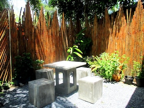 A garden with a bamboo fence, a concrete table, and potted plants.