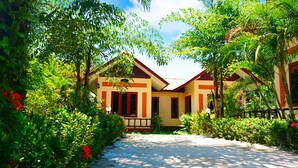 A pathway leading to a building surrounded by lush greenery and red flowers. - Happiness Resort (Krabi)
