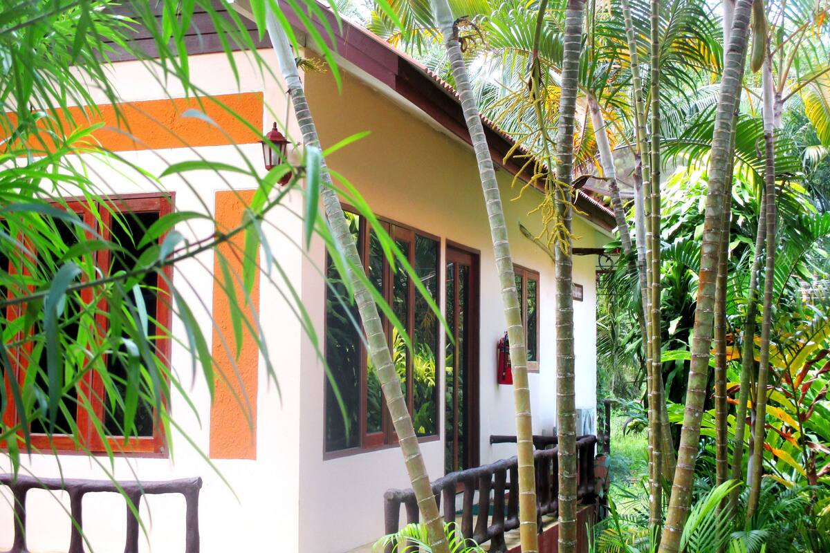 A building with a balcony, surrounded by lush greenery and tall bamboo plants.