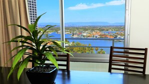A table with a potted plant, a pair of sunglasses, and a menu. The table is positioned near a window with a view of a body of water and buildings.