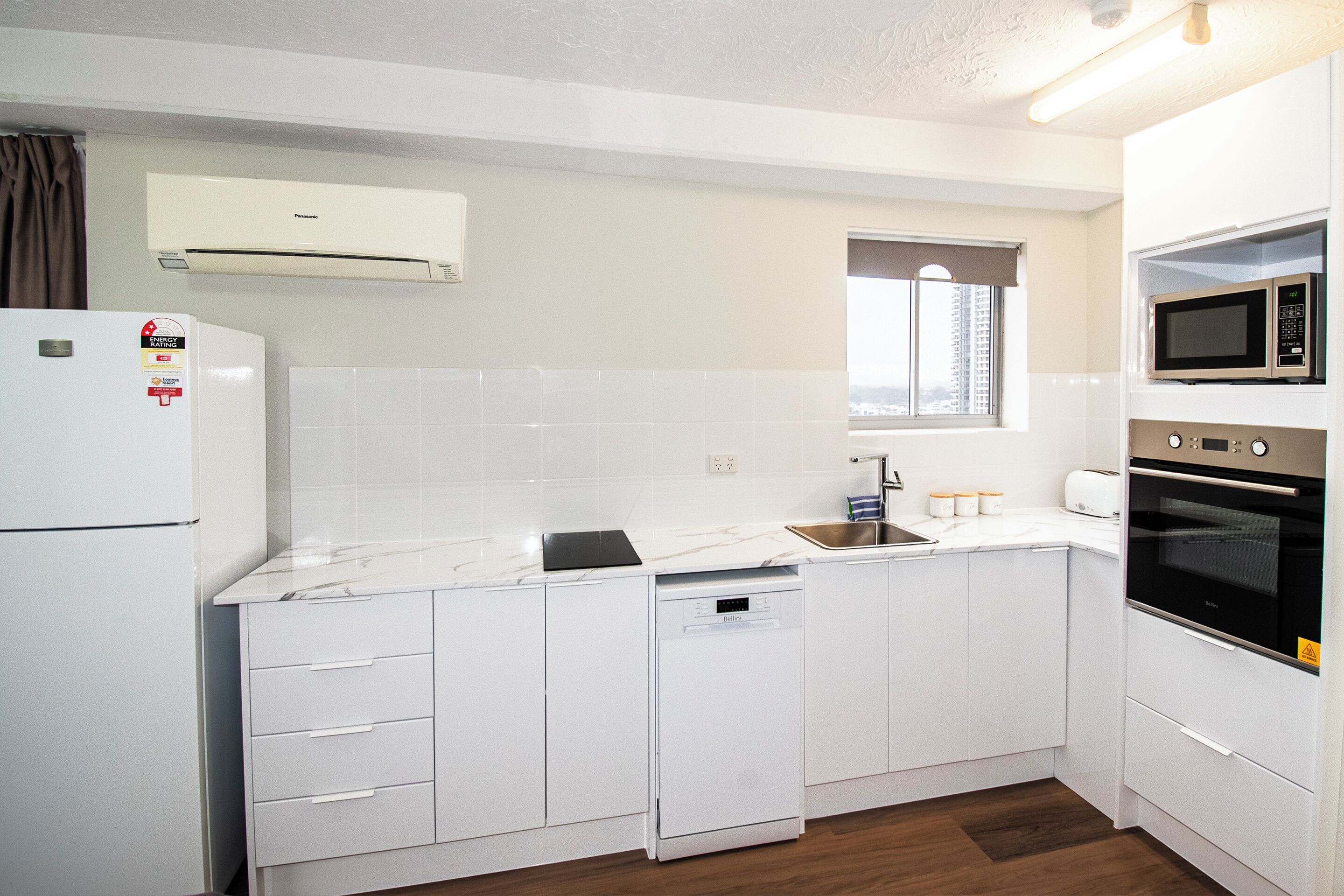 Een moderne keuken met witte kastjes, een ingebouwde vaatwasser, een magnetron en een oven.