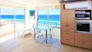 A balcony with a view of the ocean, a dining area with a table and chairs, and a kitchen with appliances.