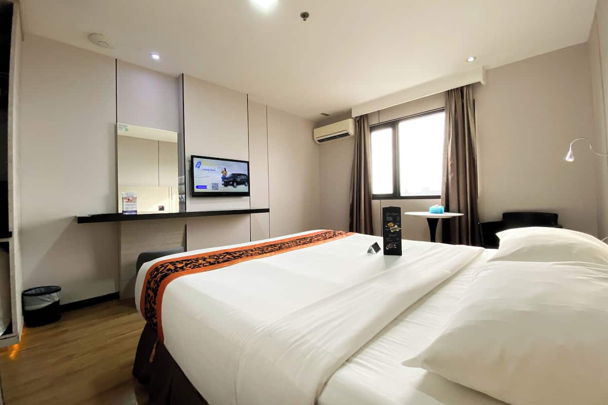 Habitación de hotel con cama, escritorio con computadora, televisor y ventana con cortinas.