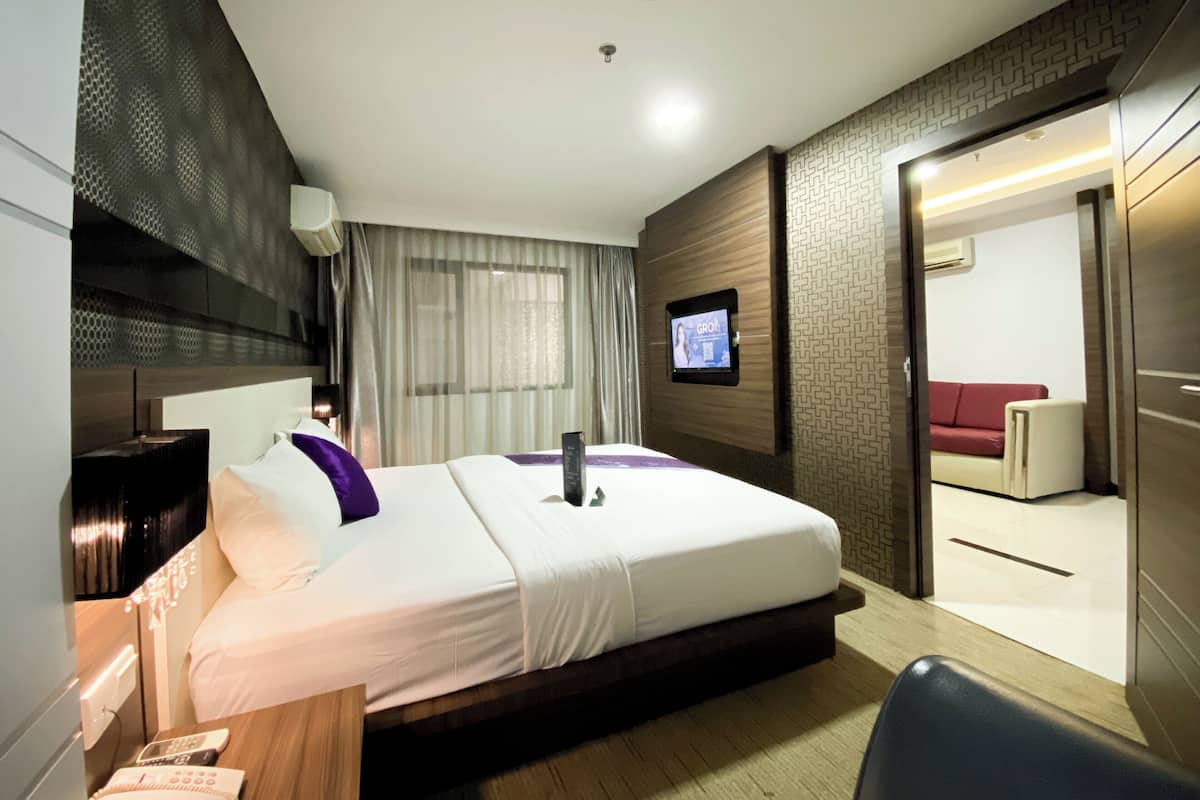 Una habitación de hotel moderna con una cama grande, un televisor montado en la pared y una zona de estar separada con un sofá rojo.