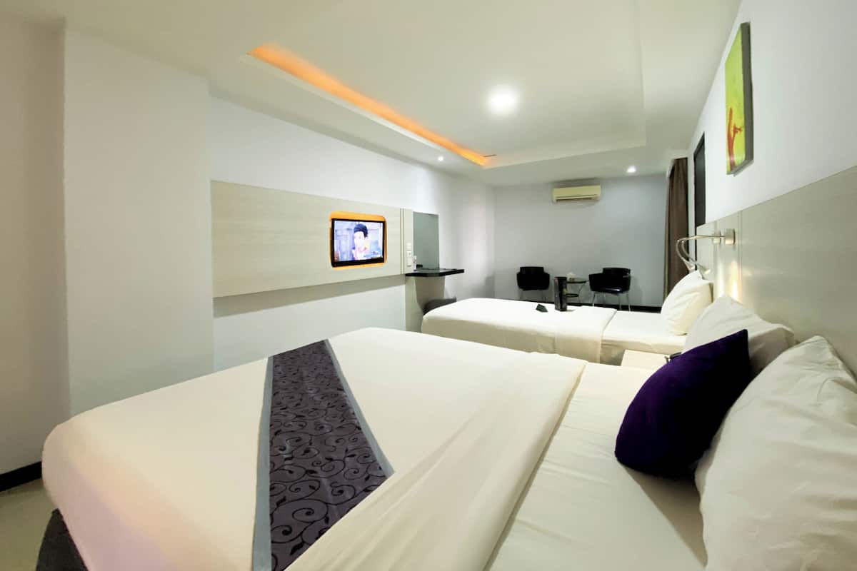 Habitación de hotel con dos camas, un televisor montado en la pared, un escritorio y una silla.