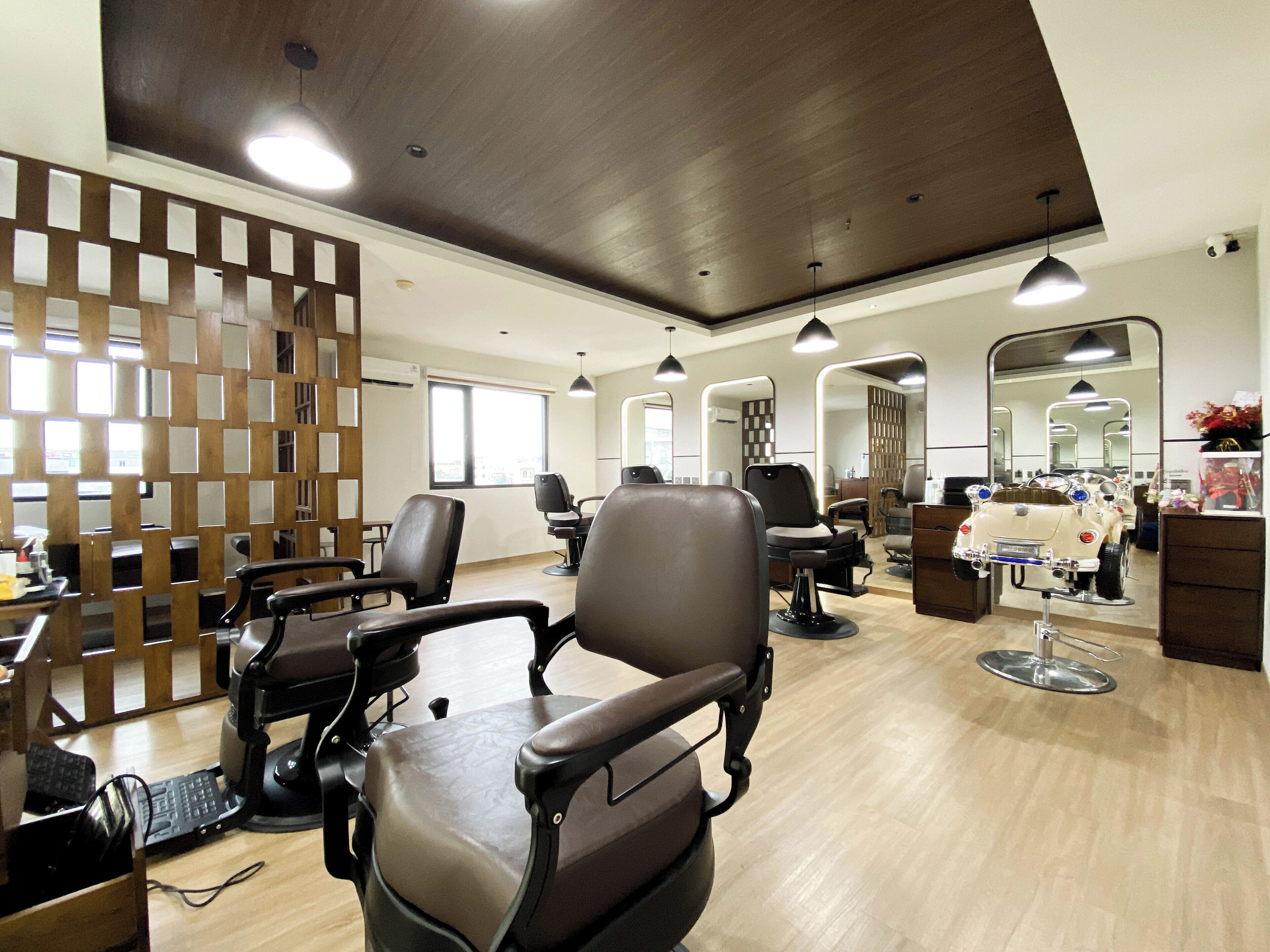 Un salón moderno con varias estaciones de peluquería, un separador de madera y un espejo grande.