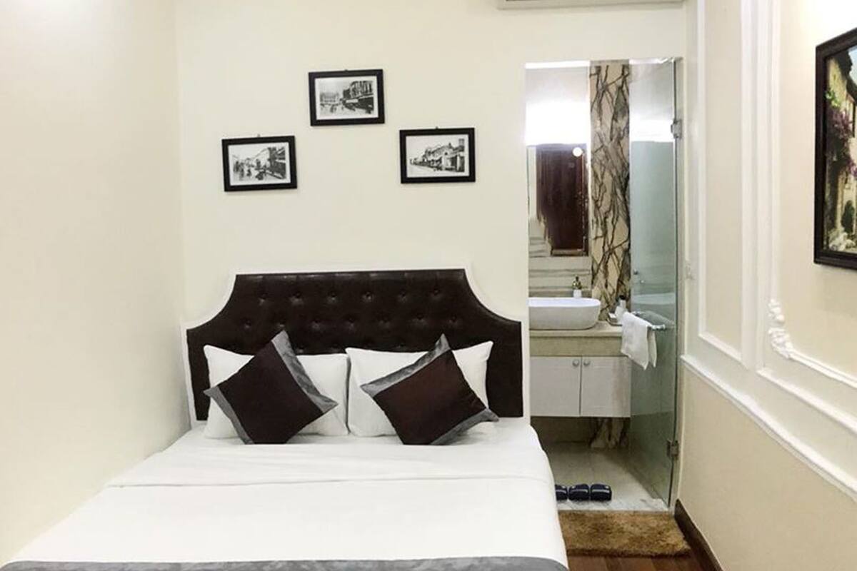 A bedroom with a bed, a headboard, a bedside table, a mirror, and a small bathroom with a sink and a towel.