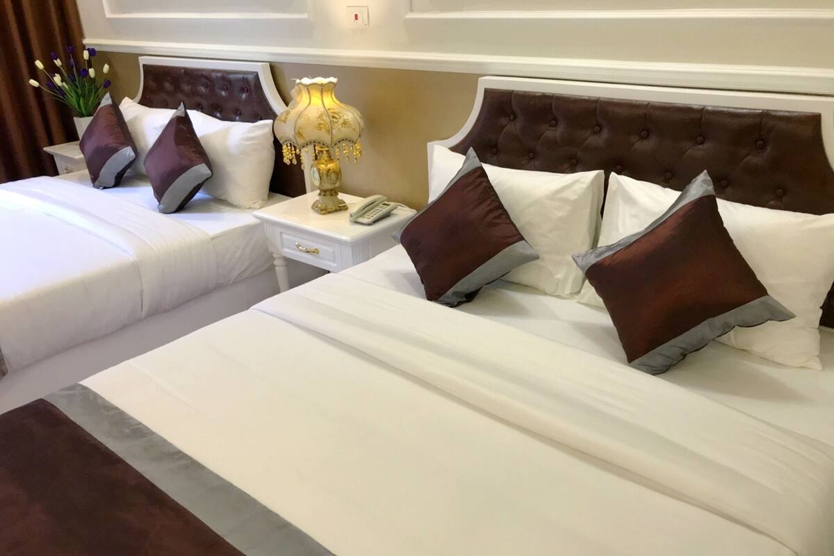 A hotel room with two beds, a nightstand with a lamp, and a plant.
