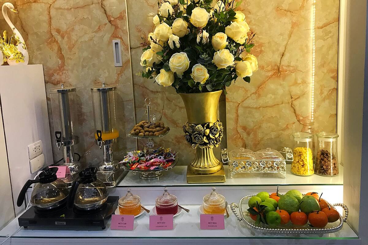 A display of food and drink items, including a vase of yellow roses, a tray of cookies, and jars of jam.