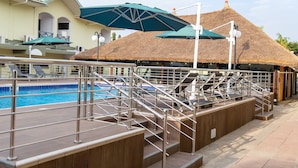 A pool area with a thatched-roof structure, a diving board, and a staircase leading to a higher level. - Sunlodge Hotel (Accra)