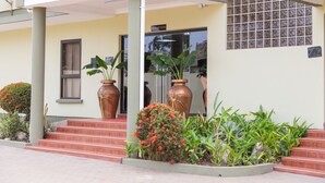 A building entrance with steps leading up to a door marked "RECEPTION," large potted plants, and a small window. - Sunlodge Hotel (Accra)