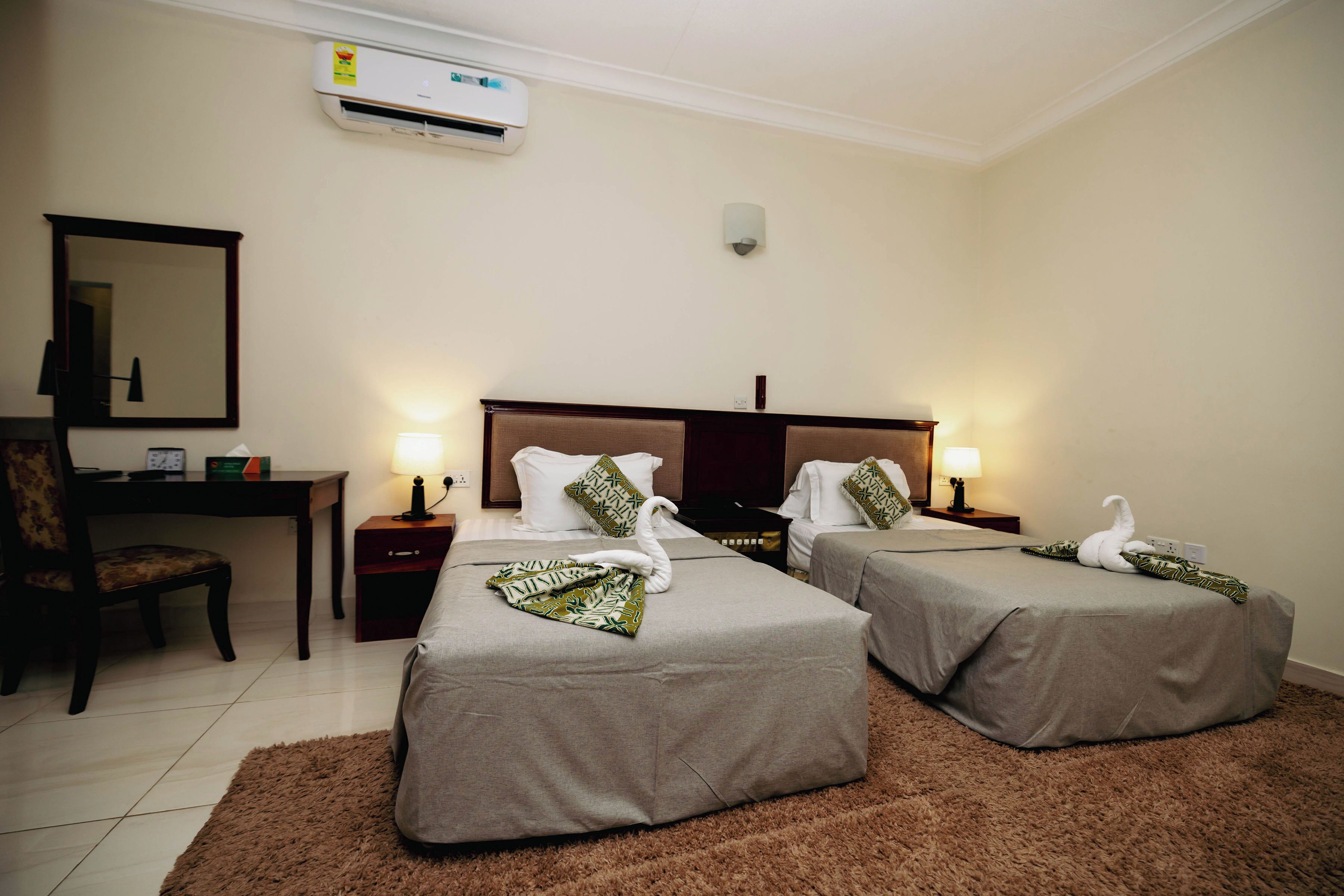 A hotel room with two beds, a desk, a chair, and an air conditioning unit.