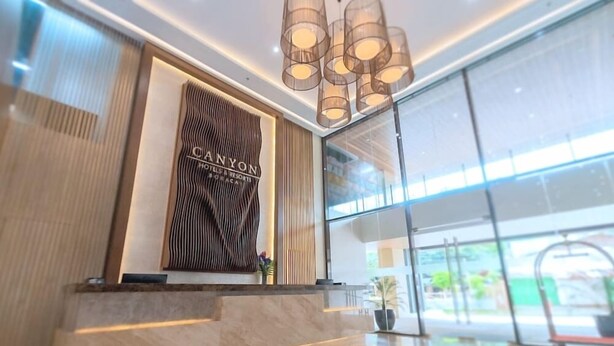Un espace d’accueil moderne doté d’un mur en verre, d’un mur en panneaux de bois sur lequel figure le texte « CANYON HOTELS & RESORTS », et d’un comptoir d’accueil en marbre.