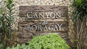 Une pancarte en bois portant l’inscription « Canyon de Boracay », fixée à un mur de pierre et entourée de verdure.