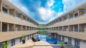 Un hôtel moderne doté d’une piscine centrale, de nombreux balcons et de plantes en pot.