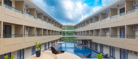 A modern hotel with a central swimming pool, multiple balconies, and potted plants.