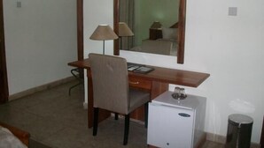 A compact hotel room with a wooden desk, a chair, a small refrigerator, a lamp, and a mirror. - Rayporsh Hotel (Accra)