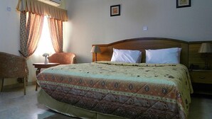 A hotel room with a bed, a chair, a nightstand, an air conditioning unit, and a window with curtains. - Rayporsh Hotel (Accra)