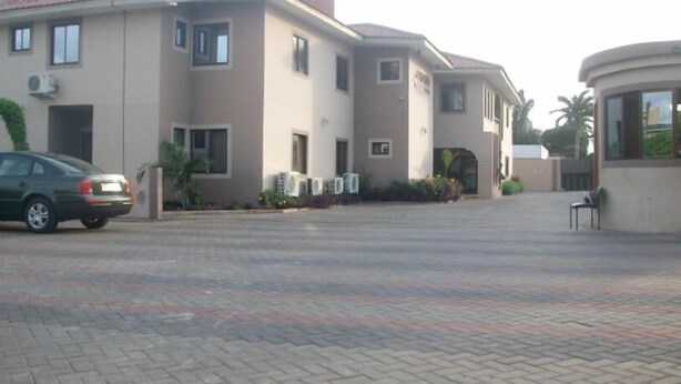 A building with multiple windows and air conditioning units, a paved driveway, and a parked car. - Rayporsh Hotel (Accra)