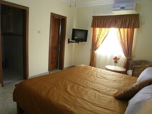 A hotel room with a large bed, a small round table, a chair, a television, and an air conditioning unit. - Rayporsh Hotel (Accra)