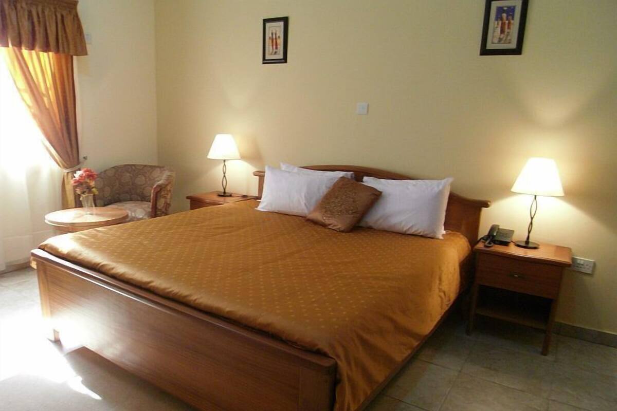 Una habitación de hotel con una cama grande, dos mesitas de noche con lámparas, una silla y una pequeña mesa redonda.