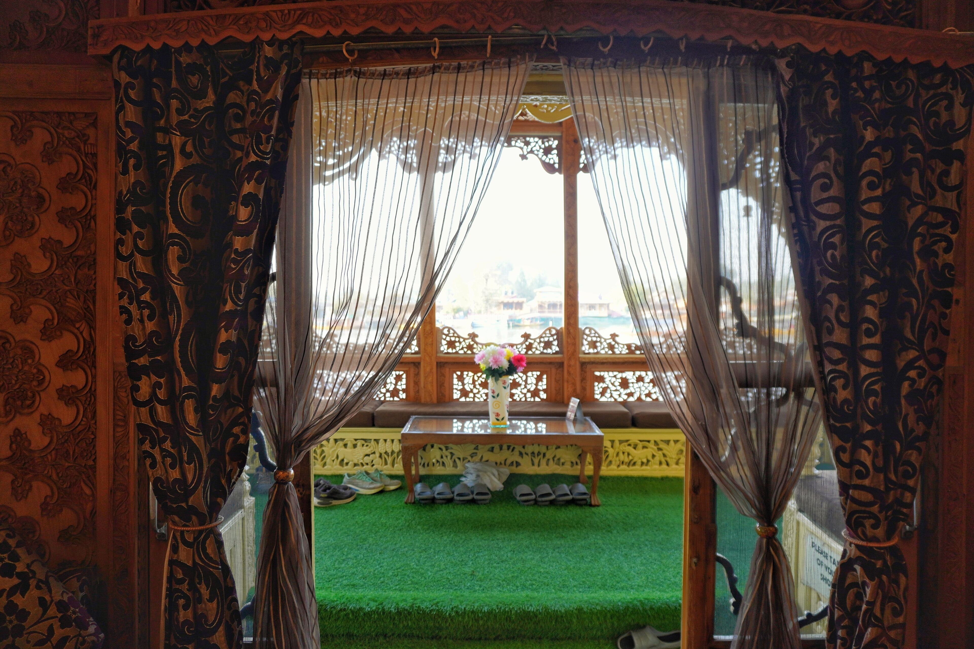 A room with a view through a window, a wooden bench, and a table with shoes and a vase.