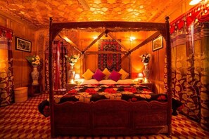 A four-poster bed with a floral bedspread, surrounded by ornate decor and a patterned carpet. - Swan Group Of Houseboats (Srinagar)