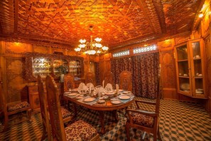 A dining area with a round table set for four, surrounded by ornate chairs. - Swan Group Of Houseboats (Srinagar)