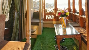 An ornate room with a glass table, a sofa, and a view through a lattice window. - Swan Group Of Houseboats (Srinagar)