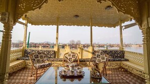 A luxurious outdoor seating area with ornate furniture and a table set for tea, overlooking a body of water. - Swan Group Of Houseboats (Srinagar)