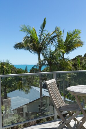 A balcony with a glass railing, a wooden chair, and a table. - Waiheke Island Resort (Waiheke Island)