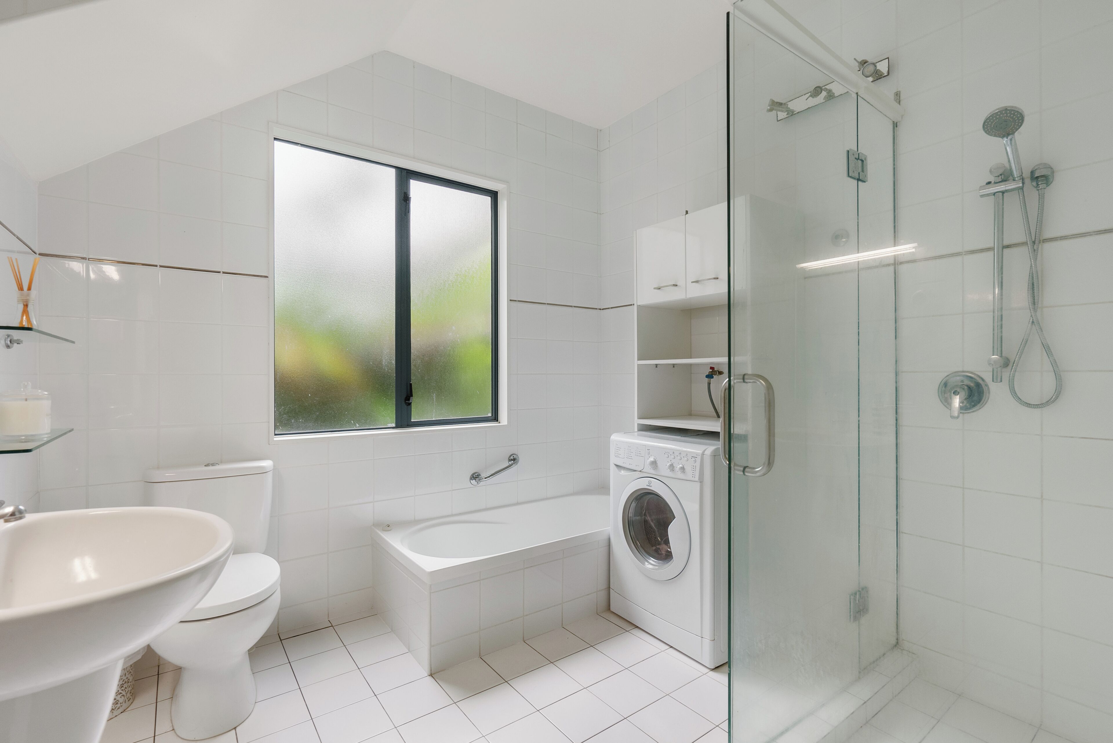 Un baño moderno con inodoro, lavabo, bañera, lavadora y ducha con mampara de vidrio.