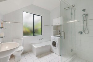 Un baño moderno con inodoro, lavabo, bañera, lavadora y ducha con mampara de vidrio.