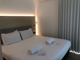 Una habitación de hotel con una cama bien hecha, un cabecero con estampado de hojas y una lámpara de pared.